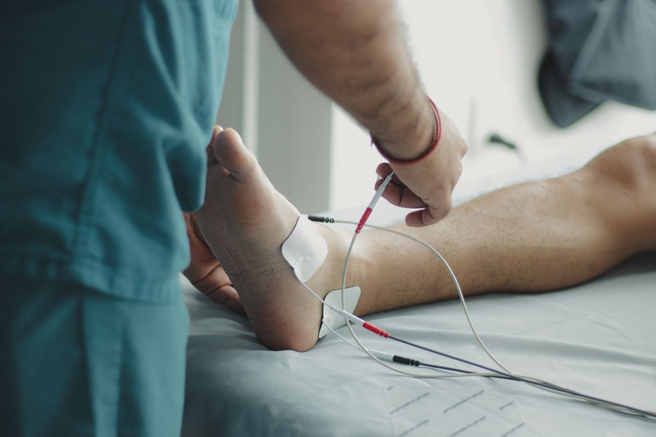Så hjälper vi dig Close-up of a healthcare worker examining a patient's foot with medical equipment in a hospital setting.