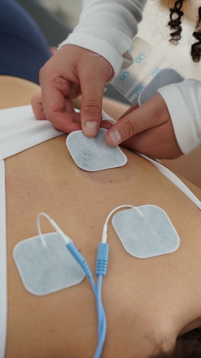 Tjänster Hands applying electrotherapy pads on the back for muscle stimulation.